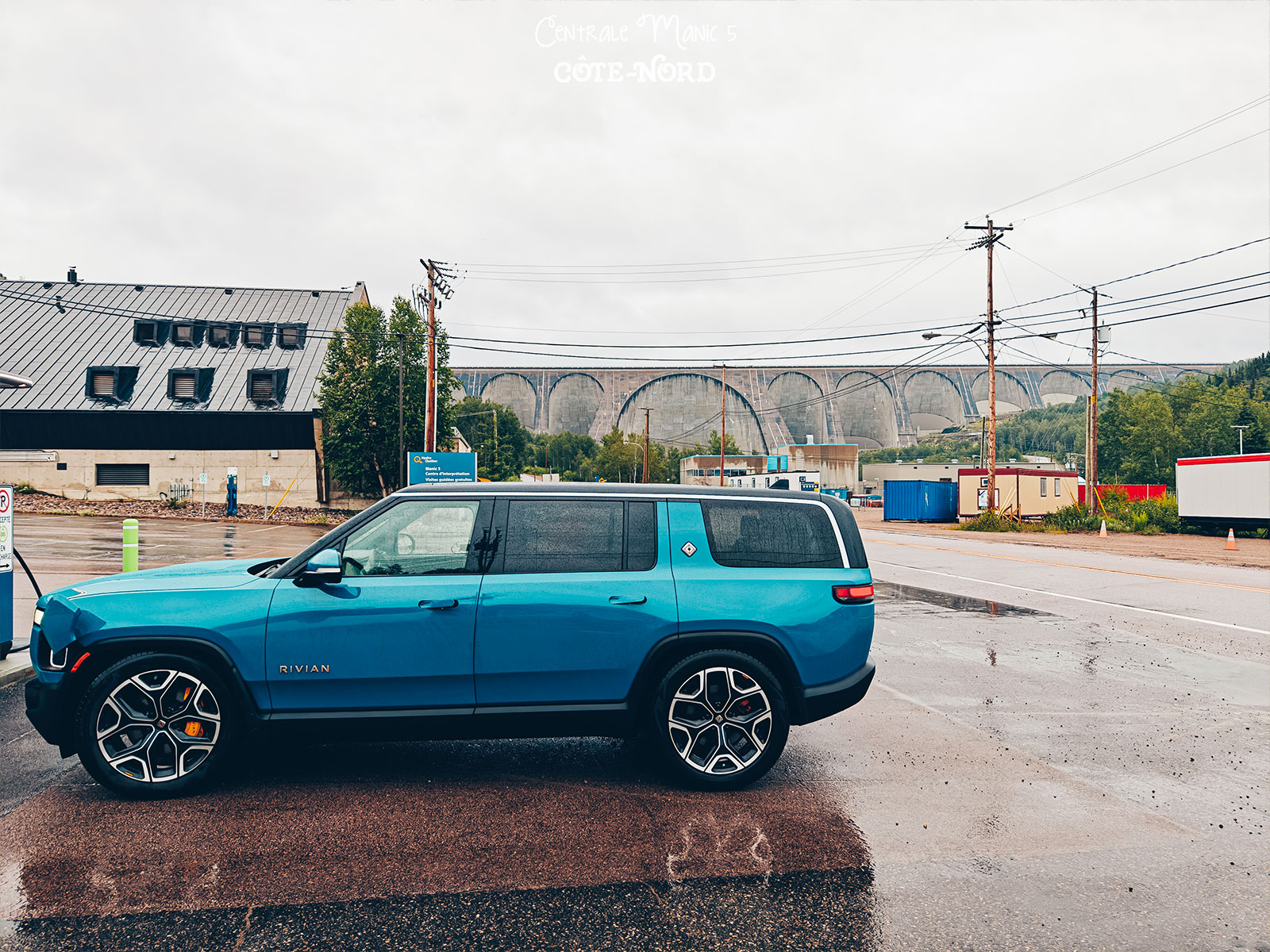 Le Rivian branché à une borne de recharge sur un stationnement mouillé, devant le barrage
