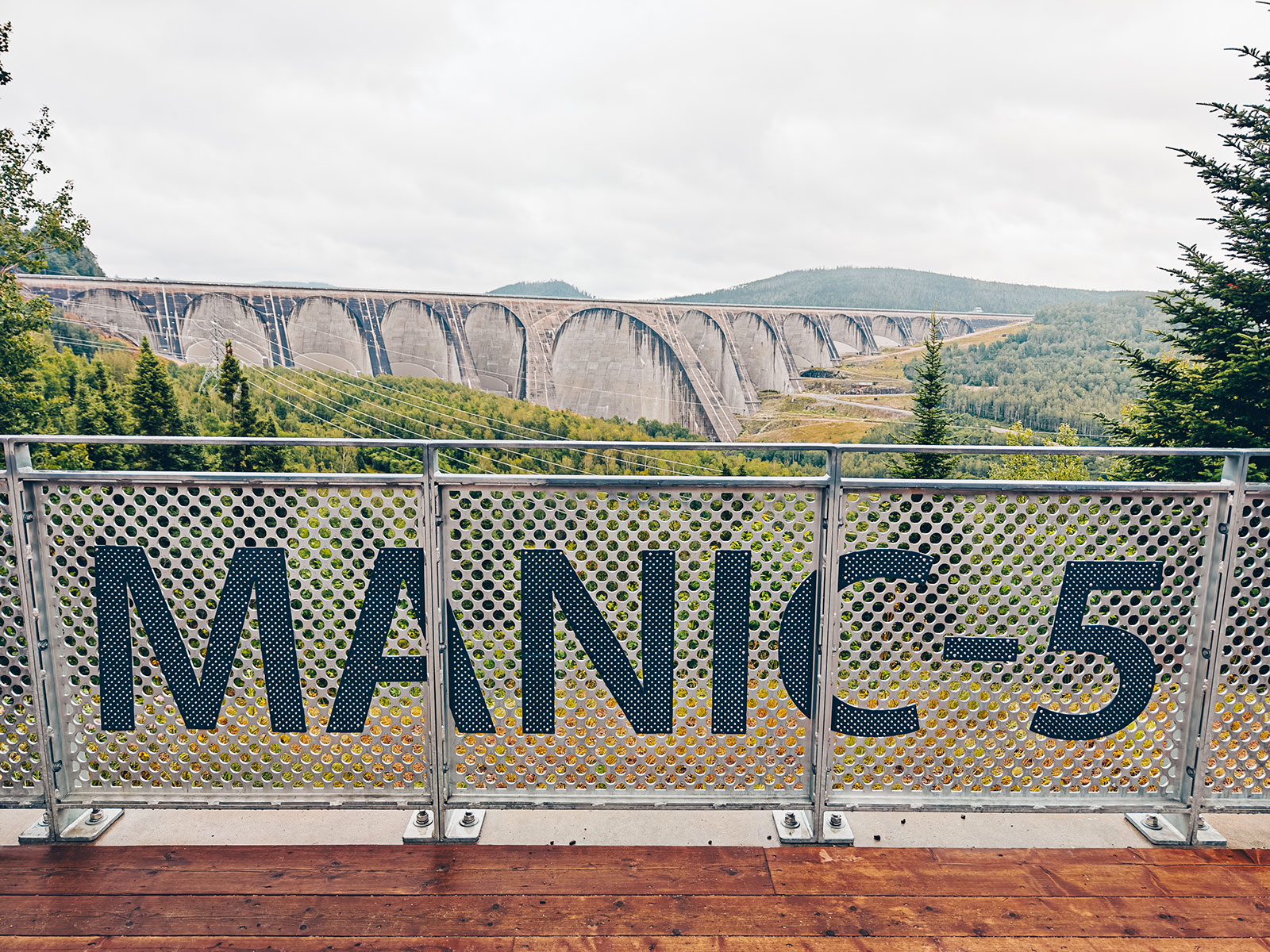 Le barrage Daniel-Johnson vu depuis le belvédère, derrière un garde-corps de tôle perforée marqué Manic-5
