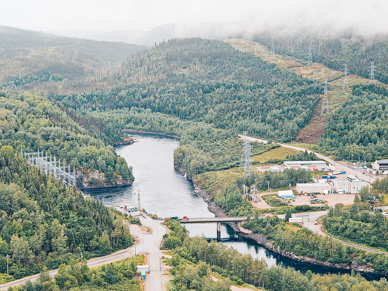 Vue plongeante sur la vallée : la rivière, un pont routier et les installations en aval