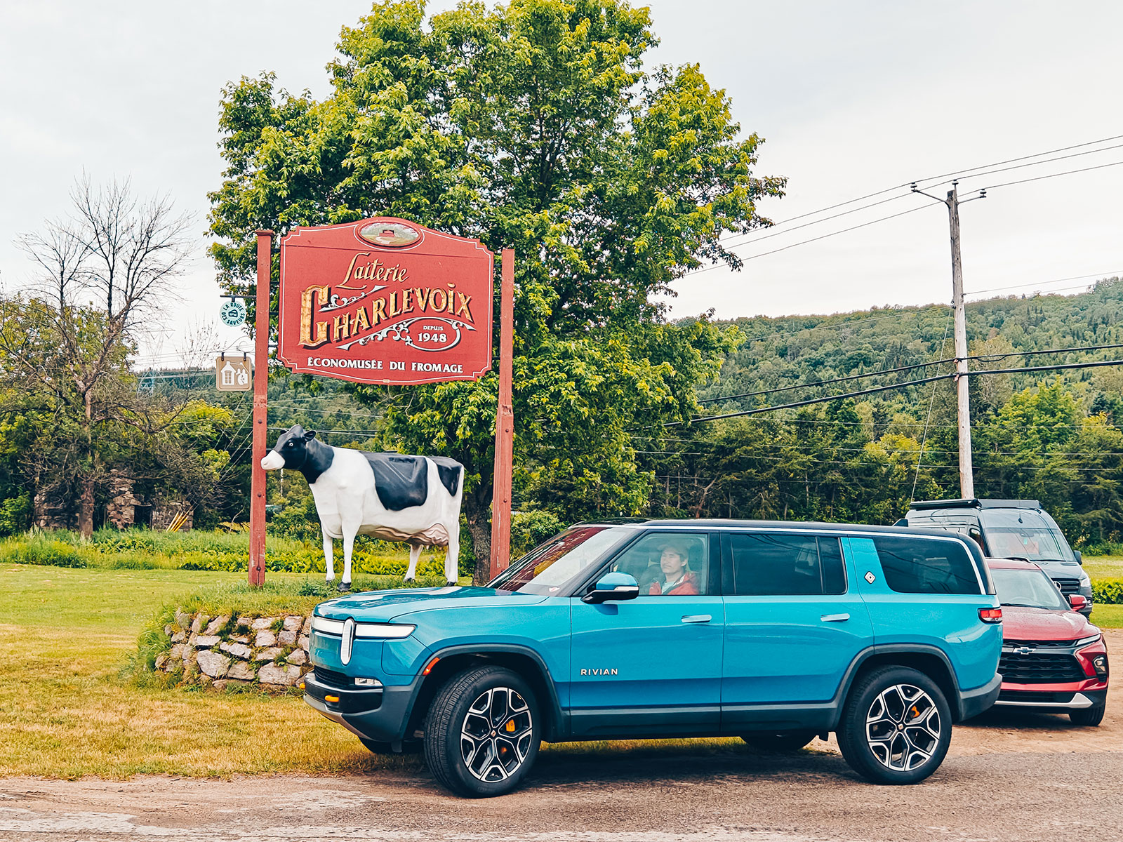L’enseigne de la Laiterie Charlevoix avec une vache en modèle et le Rivian garé devant
