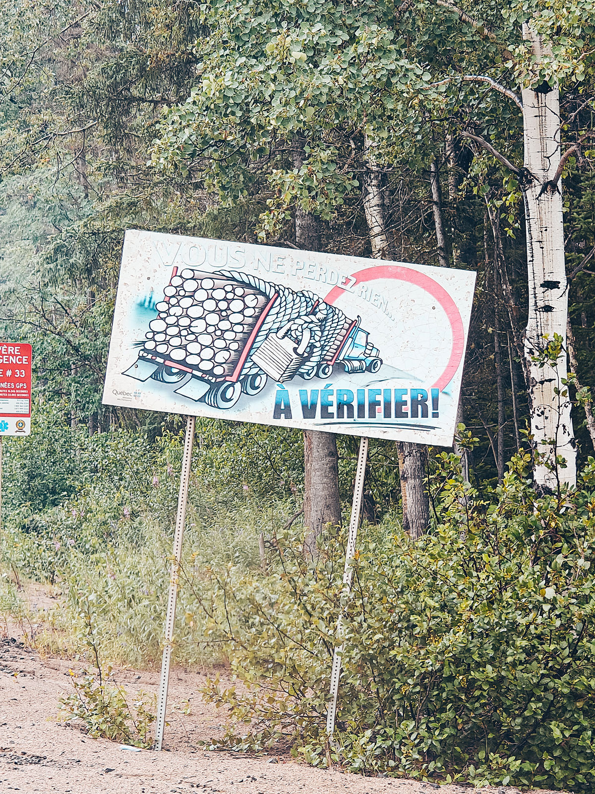 Un panneau au bord de la route montrant un camion chargé de billots et le mot « À vérifier »