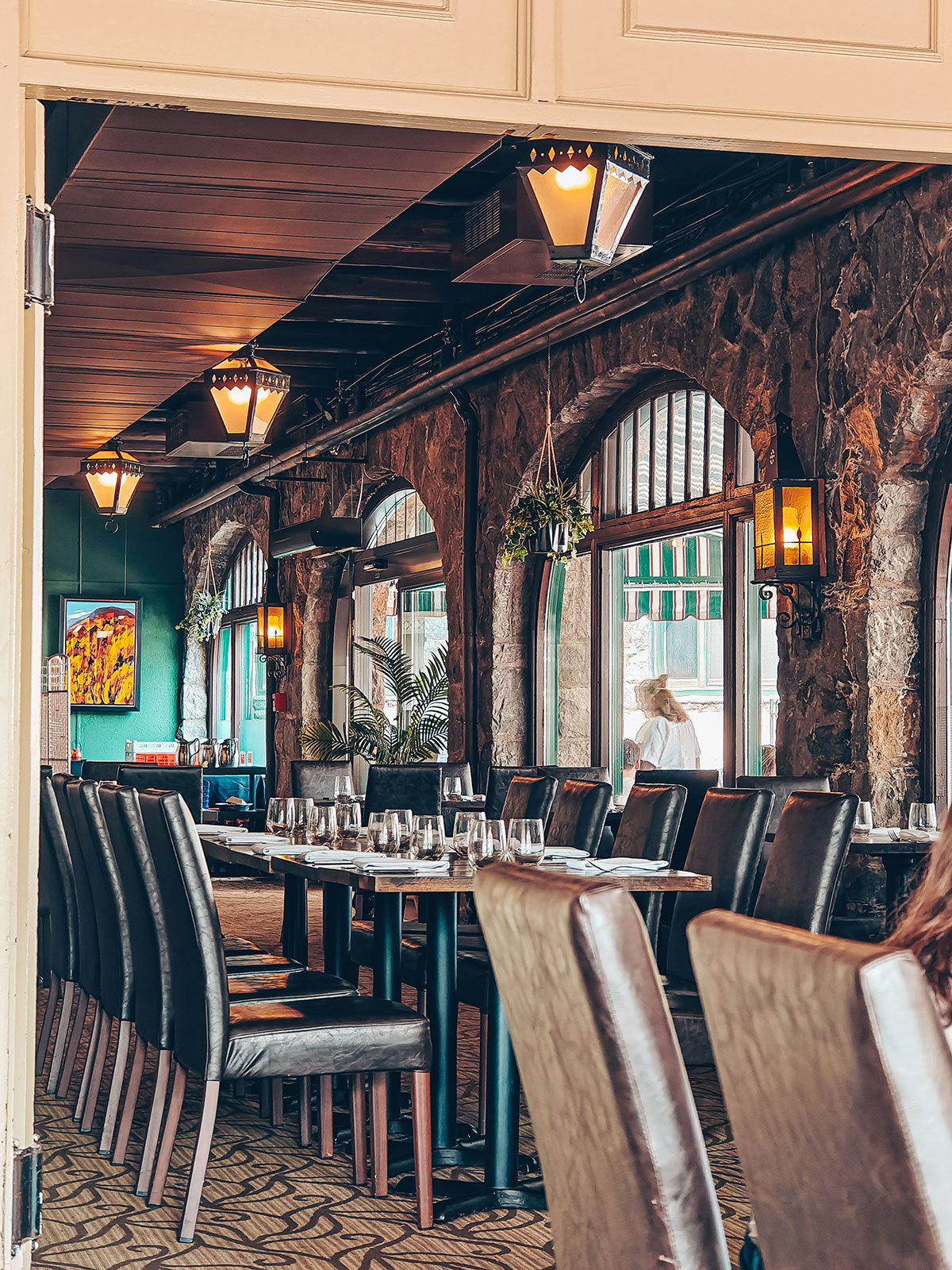La salle du restaurant : mur de pierre, fenêtres en arc, poutres et boiseries turquoise