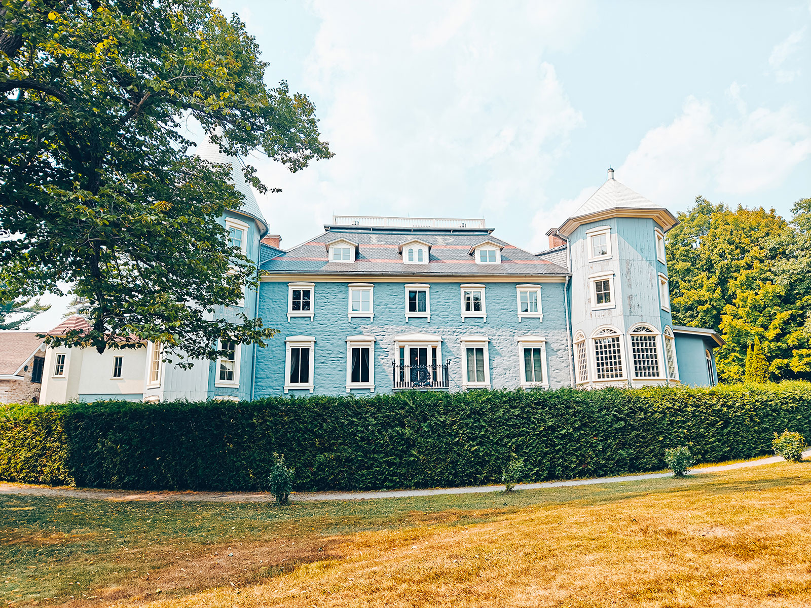 Vue large du manoir derrière sa haie, au bout de la pelouse