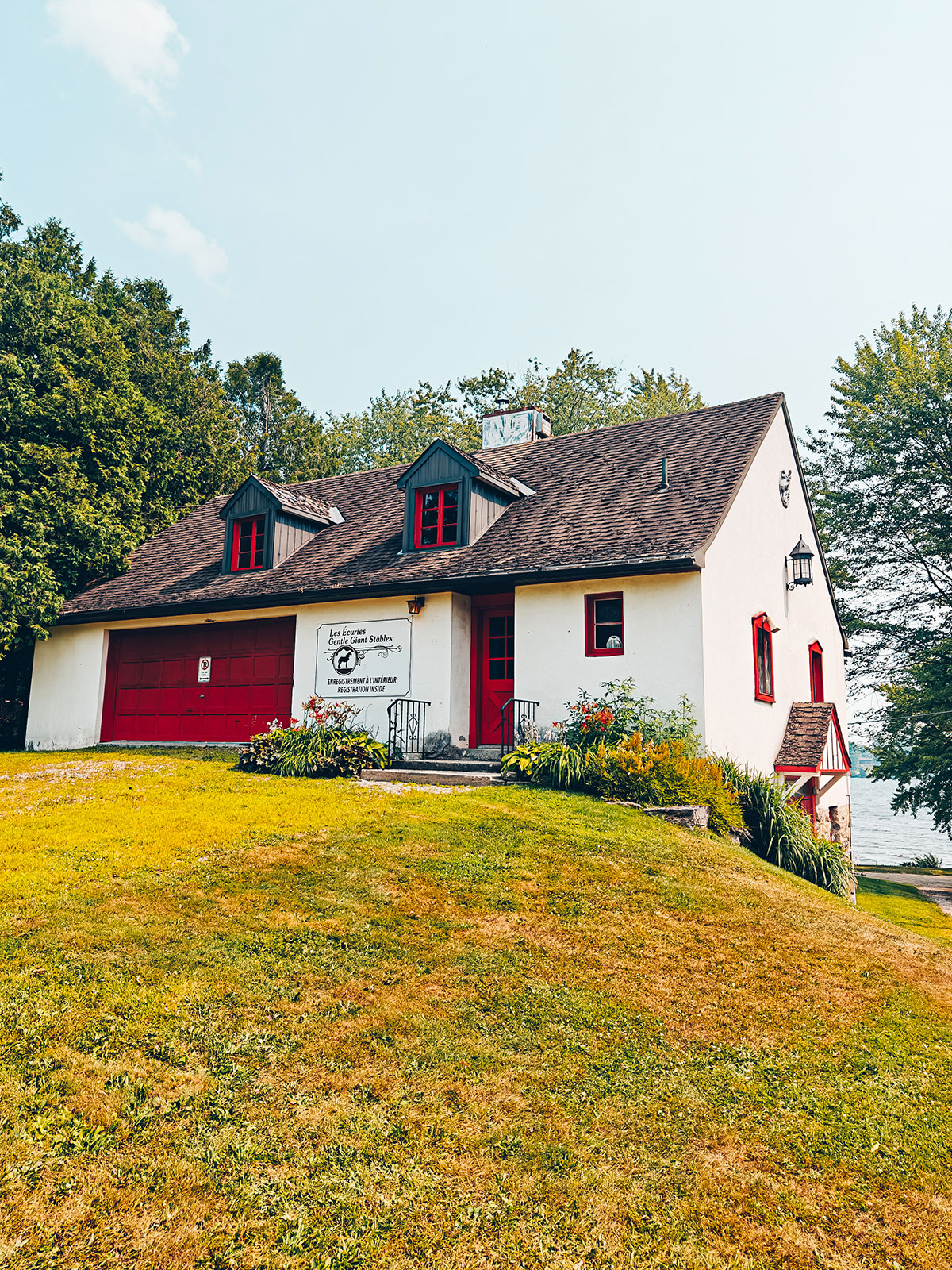Une maison blanche à toit sombre et portes rouges, sur la pelouse