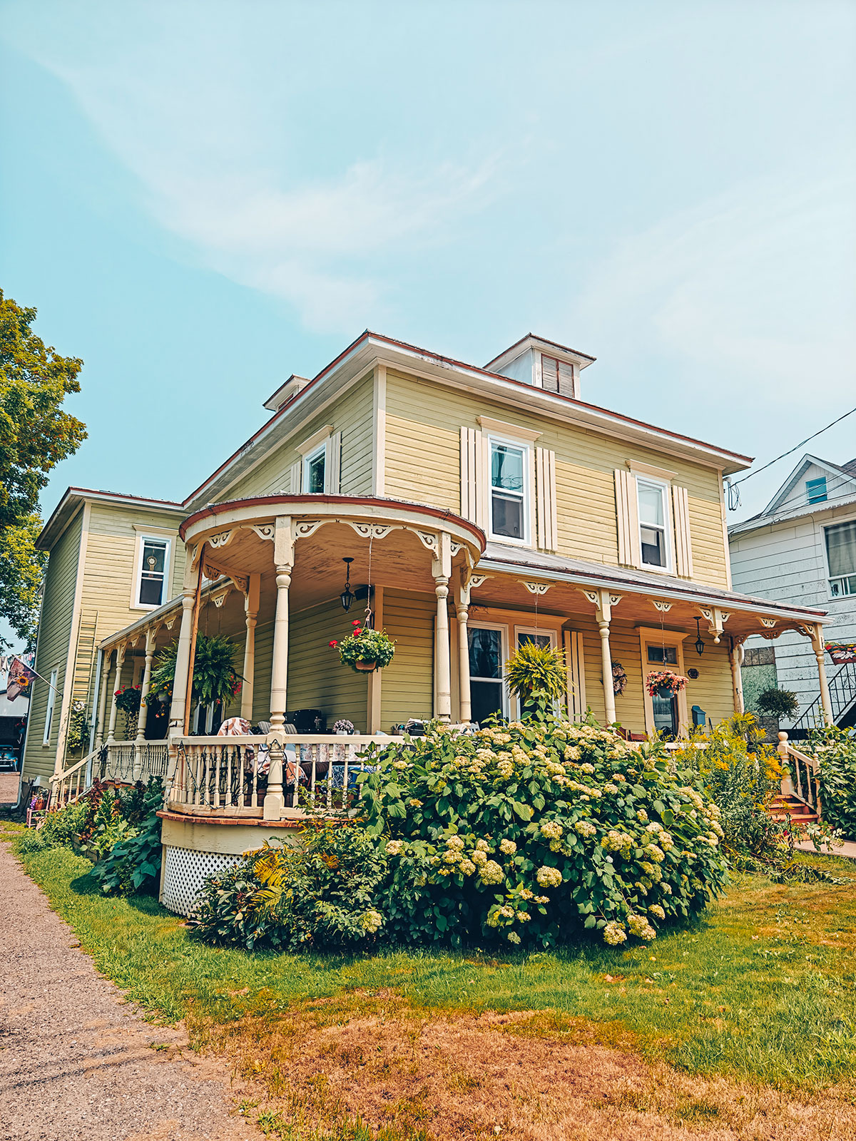 Une maison victorienne jaune, sa galerie faisant le tour de la façade