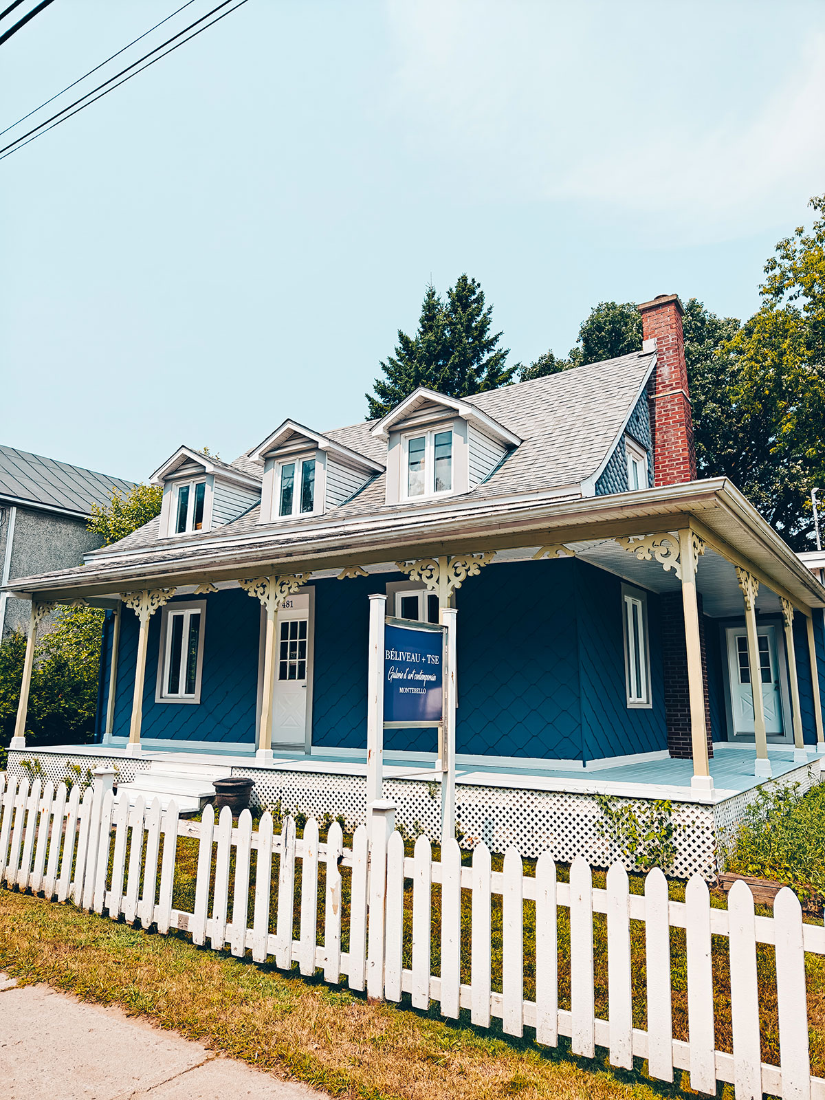 Une maison bleue à galerie blanche, derrière une clôture de piquets