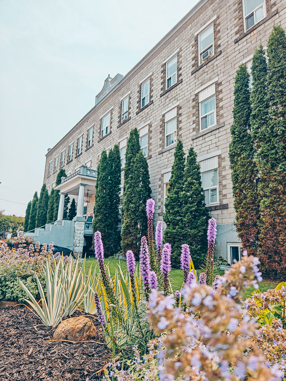 Le long bâtiment de pierre du couvent, derrière un massif de fleurs mauves
