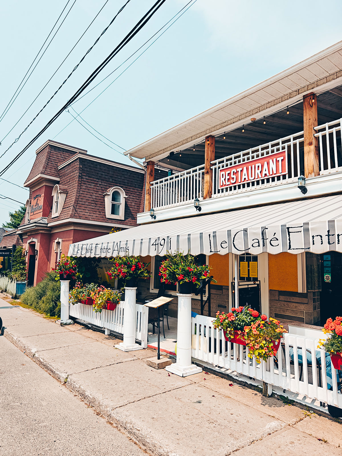 La rue principale : un bâtiment de brique rouge, l’enseigne d’un restaurant et des jardinières