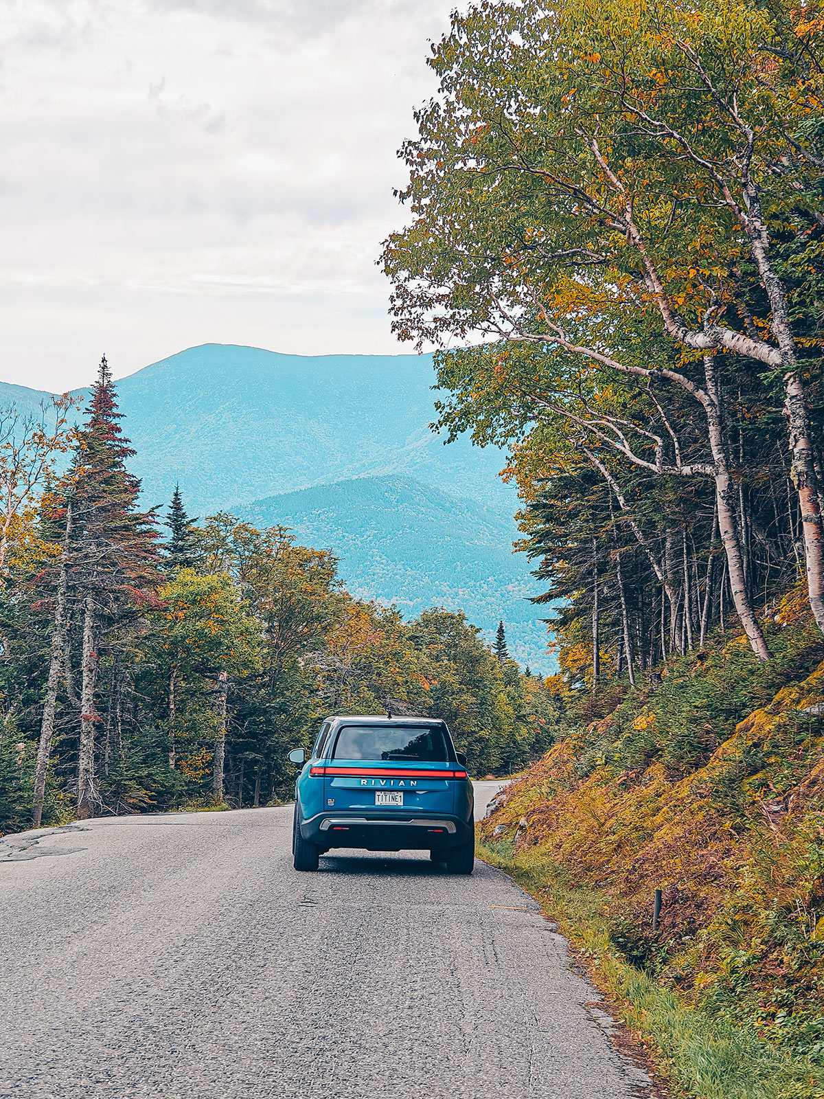 Le Rivian redescend la route de forêt, les montagnes bleues devant