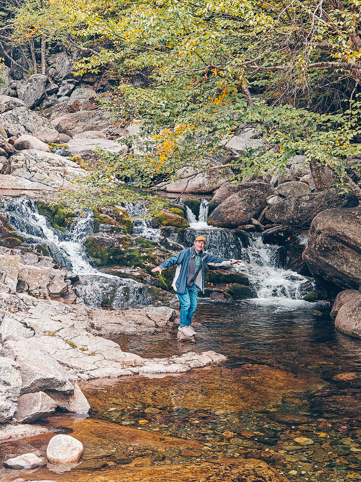 Une personne debout au milieu du ruisseau, au pied de la cascade