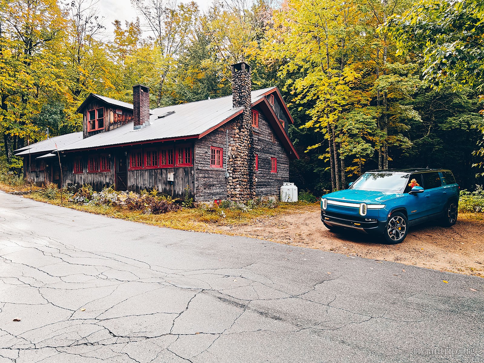 Une grande bâtisse de pierre au bord de la route, le Rivian devant